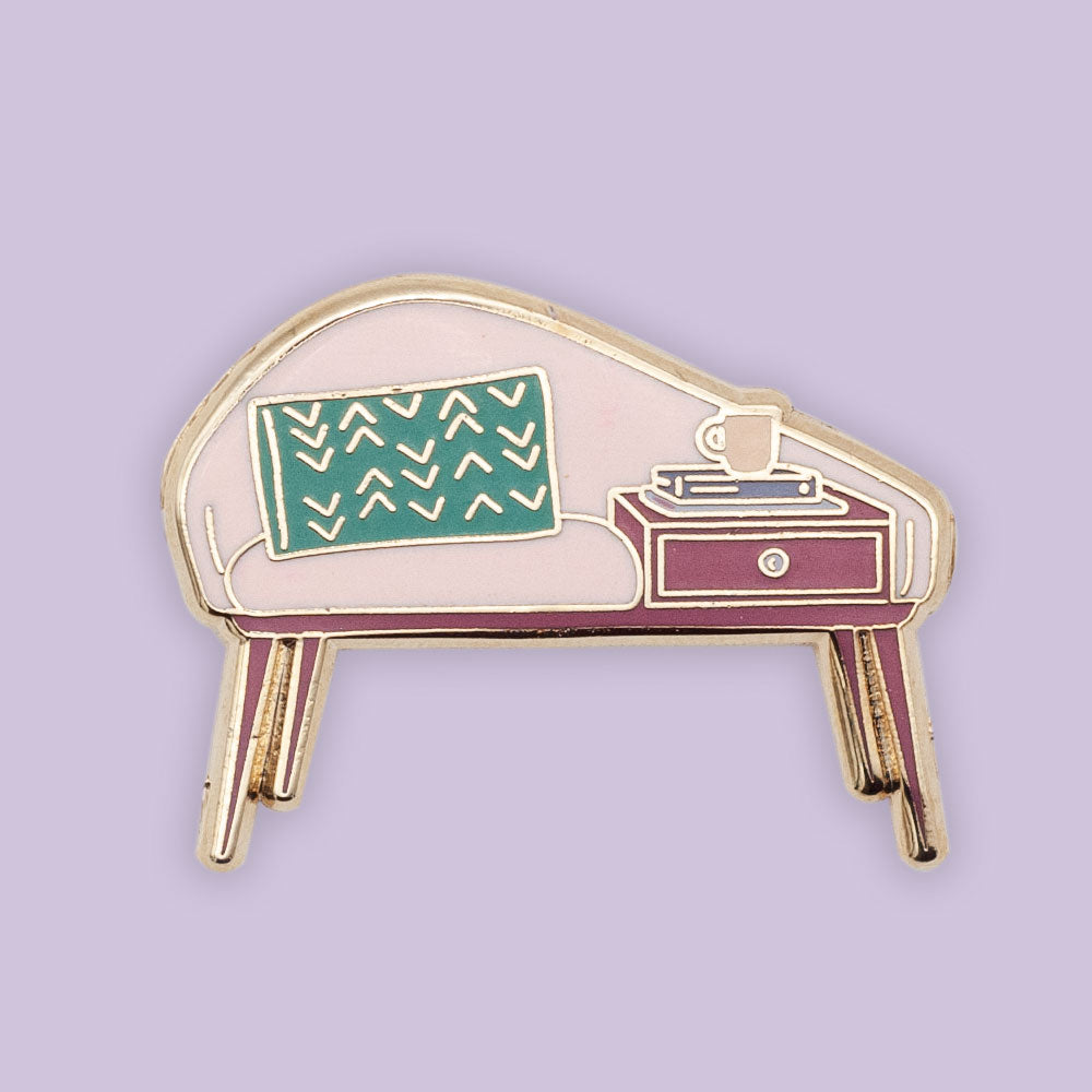 Mid-century modern bench enamel pin. gold plated with pink, teal and deep pink enamel. Pin is over purple background.