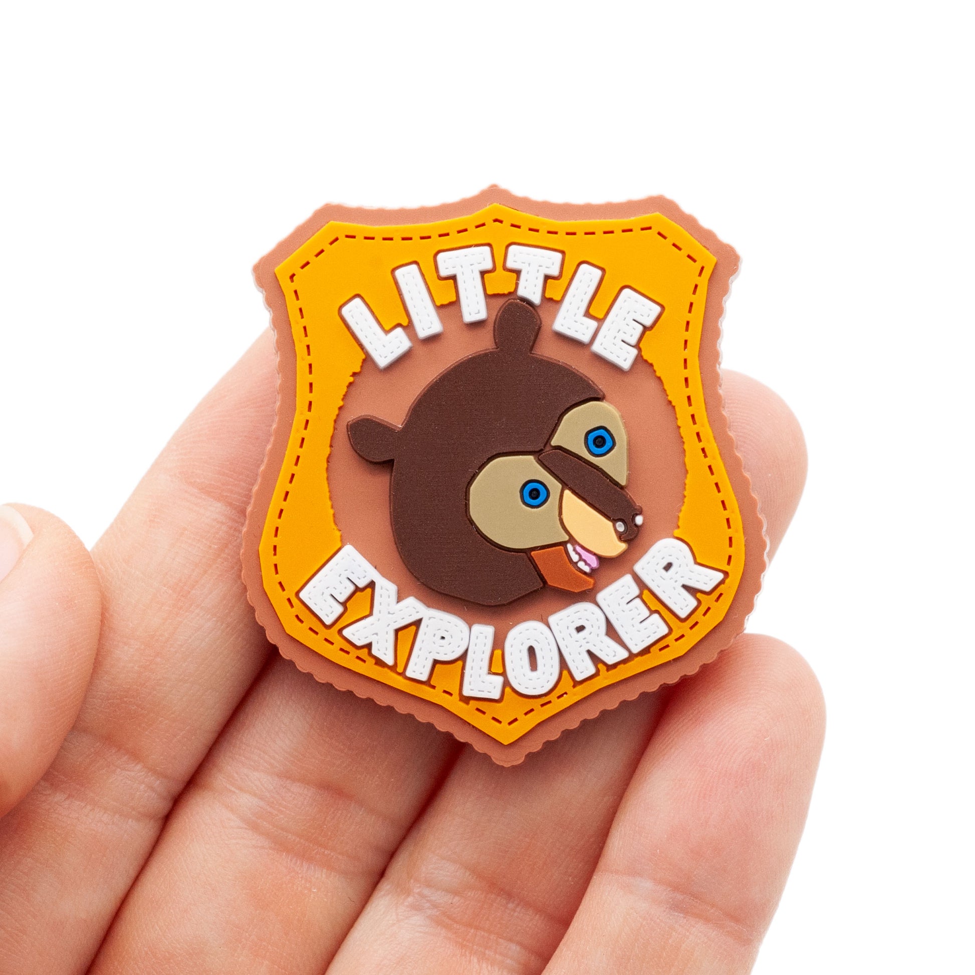 Little Explorer magnet made of soft PVC. Bown bear in the center with letter above and below bear. Colors include light brown, orange , dark brown, blue eyes, and white lettering. Lettering says "little explorer".