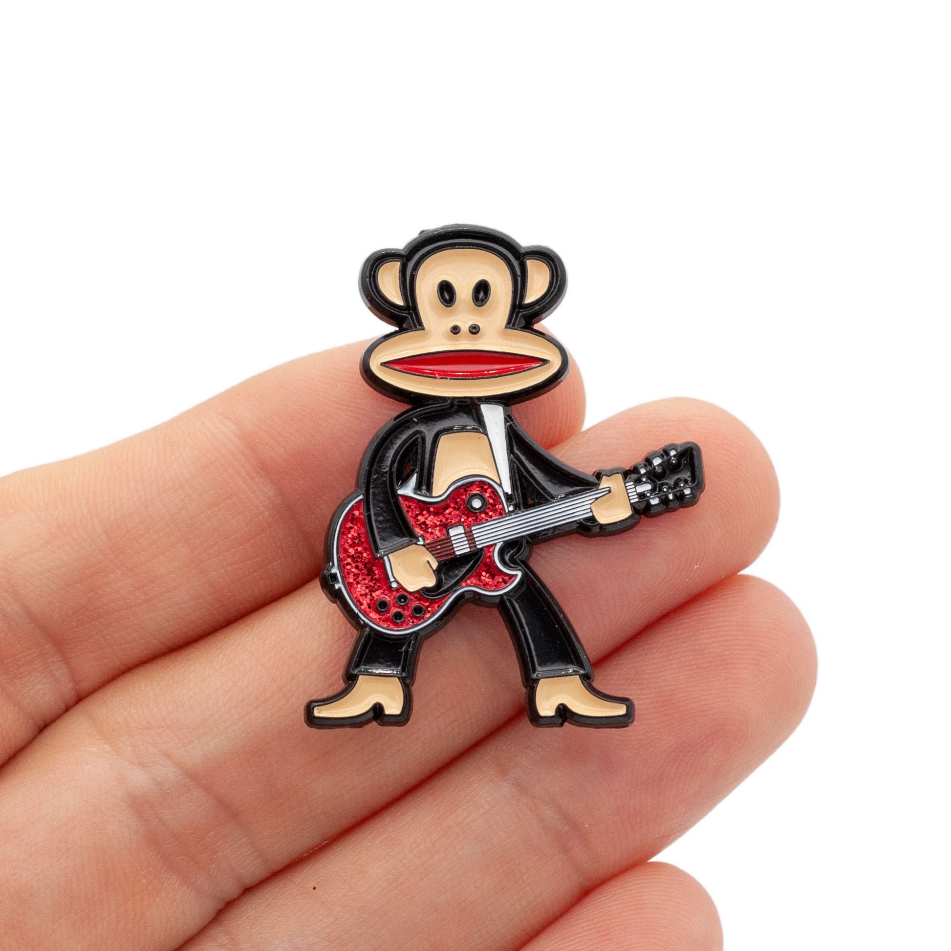 Julius the monkey playing a red glitter guiter, held by a hand against a white background.