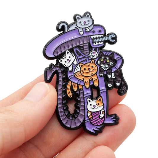 Xenomorph pin covered in cats is being held up in this photo.