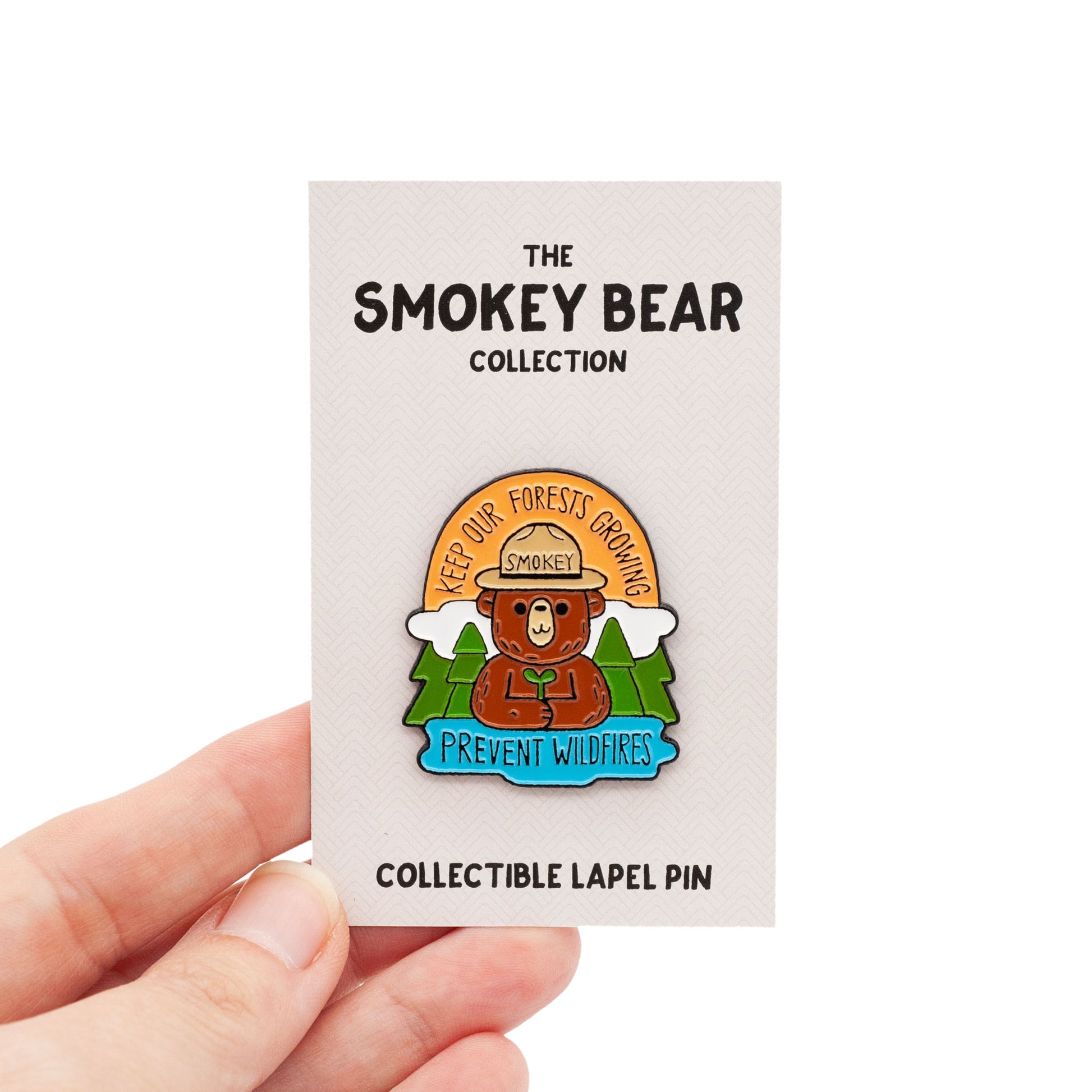 smokey bear holding a sapling, surrounded by trees. Across the top says "Keep our Forests Growing" and on the bottom it says "prevent wildfires". On backing card over a white background.