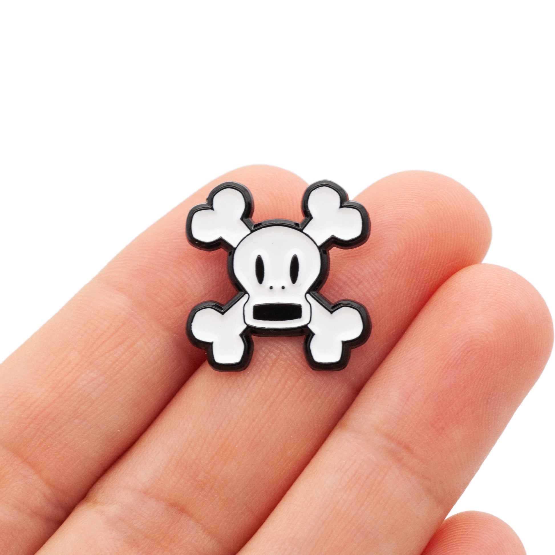 Skurvy is a soft enamel pin of white crossbones with an open mouth. shot being held by a hand over a white background.