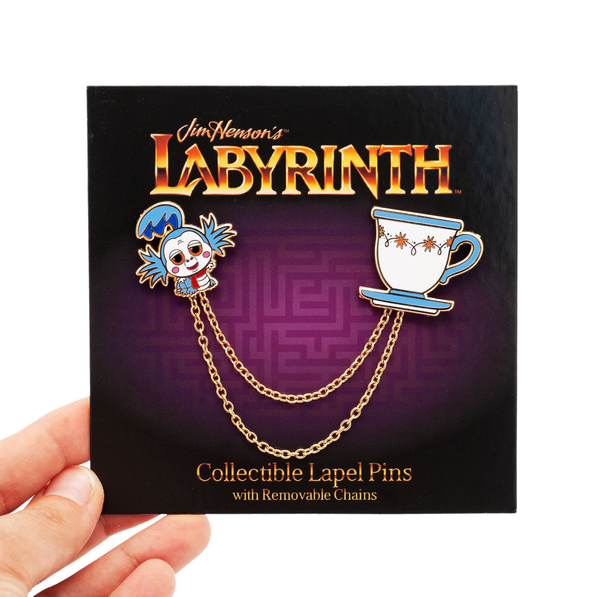 the worm and teacup lapel pins and connecting chains, on purple labyrinth backing card. card is being held by a hand against a white background.