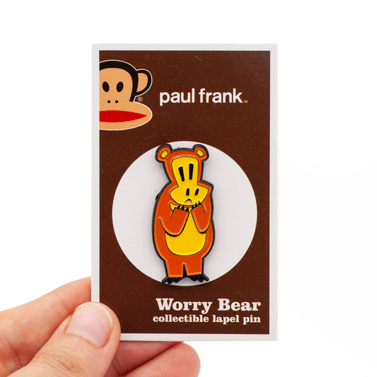 Worry Bear is a brown bear with a yellow tummy. He has a worried look on his face, since he is always worried. Pin is on brown and white backing card, held by a hand over white background.